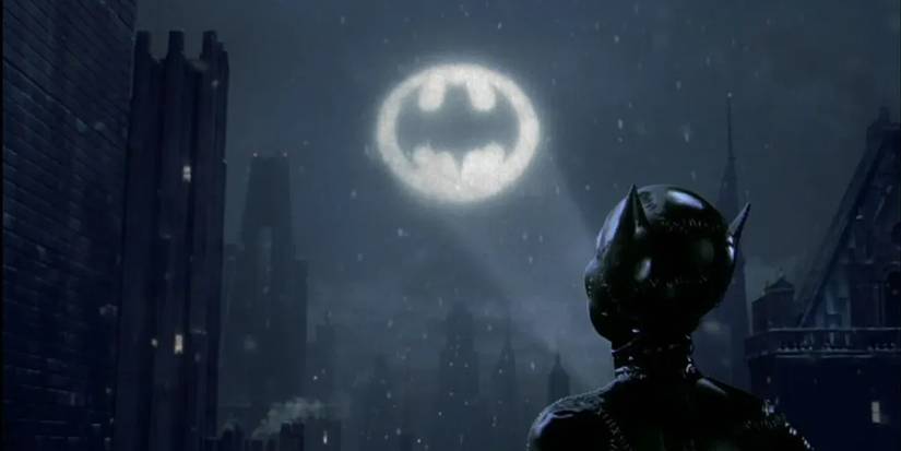 Catwoman looking up at Batman logo shining in the grey night's sky in Batman Returns