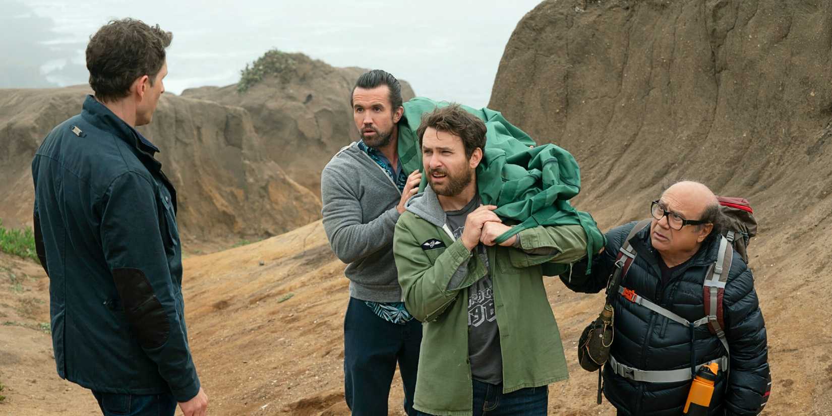 Dennis watches as Mac, Charlie, and Frank carry a corpse up a mountain in It's Always Sunny in Philadelphia.