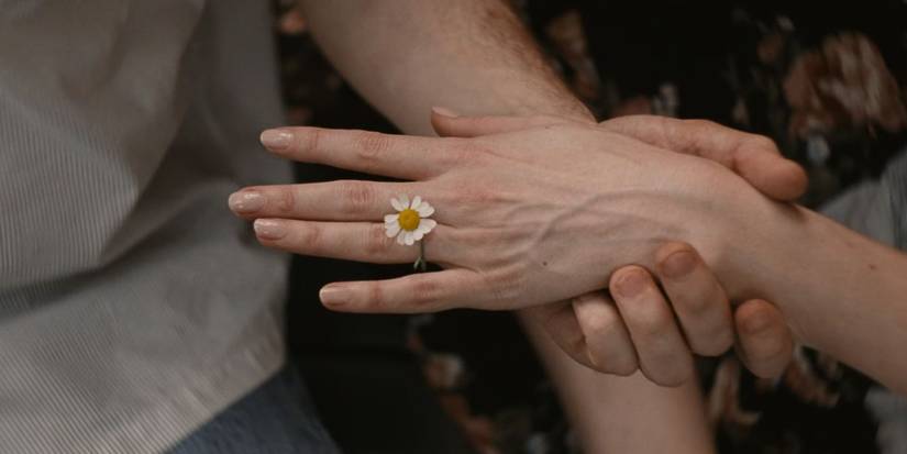 A daisy ring is slipped onto Lucy's hand by John in Materialists