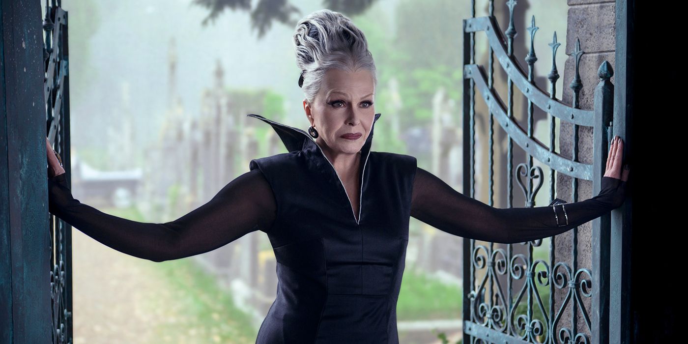 Joanna Lumley standing between open iron gates in Wednesday Season 2.