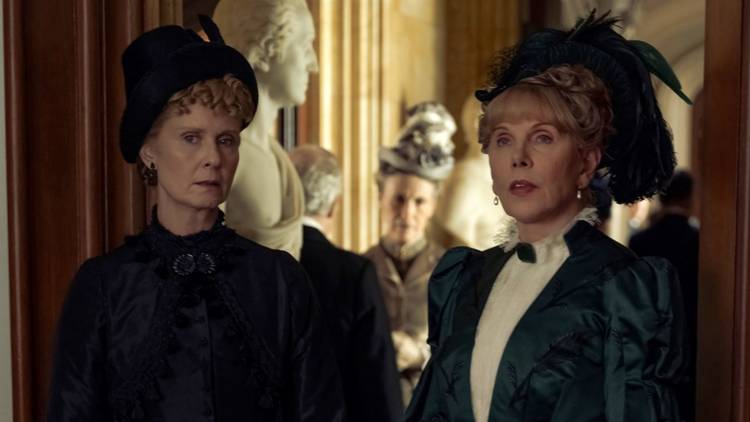 Cynthia Nixon as Ada standing next to Christine Baranski as Agnes in full dress and hats in The Gilded Age